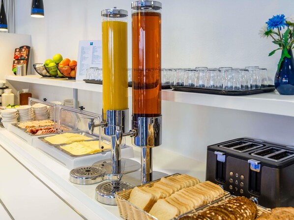 Montaje de bufé con diferentes opciones de comida, un dispensador de bebidas y un tostador.
