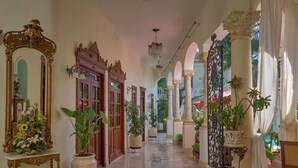 A grand hallway with ornate wooden doors, large potted plants, and a tiled floor with intricate patterns. - El Palacito Secreto (Mérida)