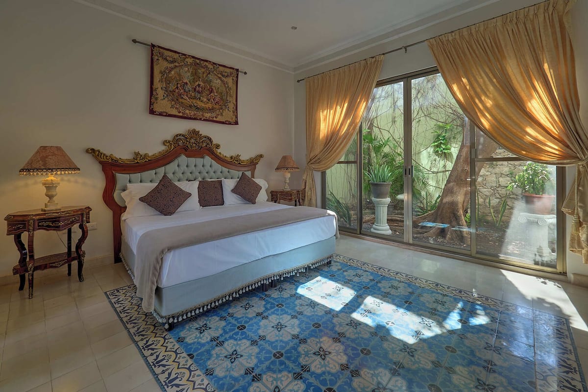 Un dormitorio amplio con una cama grande, un cabecero decorativo y vistas a un jardín a través de una puerta corrediza de vidrio.