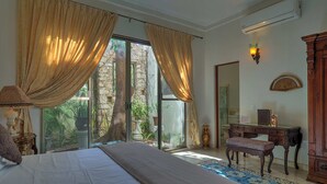 A bedroom with a large bed, a desk, a chair, and a view of a garden through a glass door. - El Palacito Secreto (Mérida)