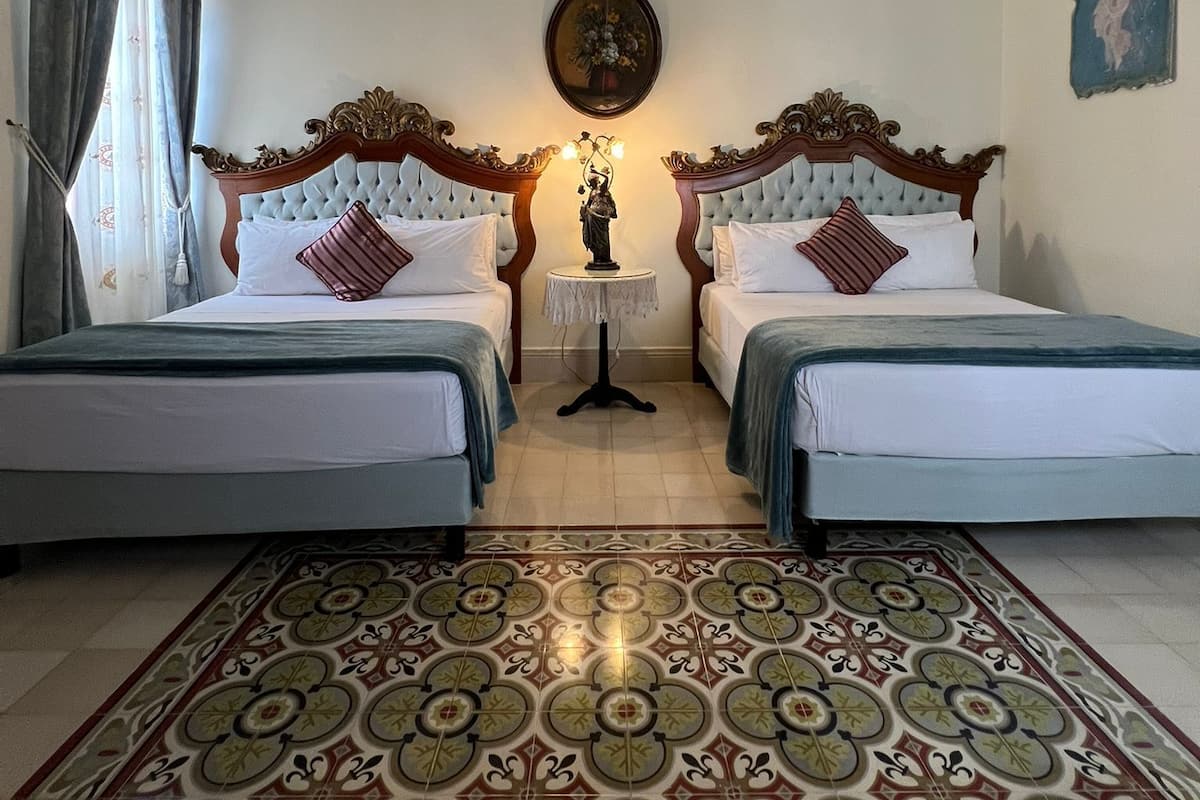 Una habitación con dos camas, una mesita con una estatua, un ventilador de techo y un suelo con diseño.