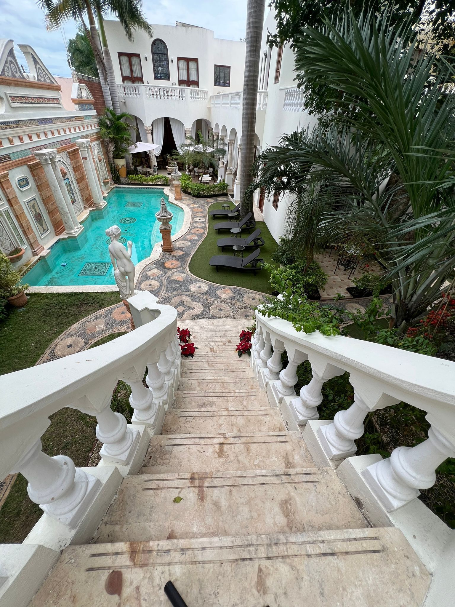 A pool area with a statue, white balustrades, and a staircase leading to a covered terrace.