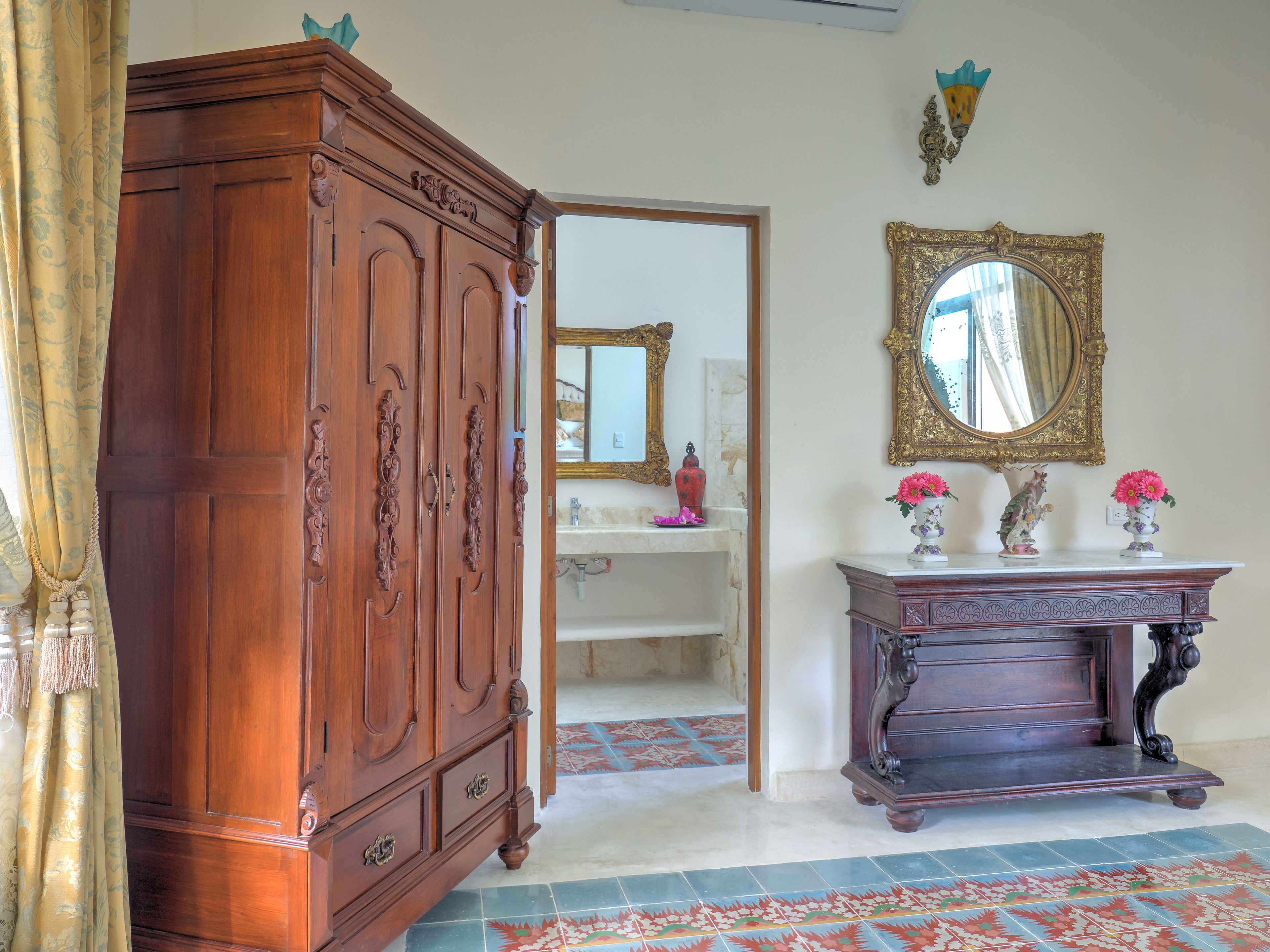 Habitación con armario de madera, tocador decorado, espejo y baldosas de piso estampado.
