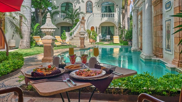 A luxurious outdoor dining area with a pool, surrounded by ornate architecture and tropical plants. - El Palacito Secreto (Mérida)