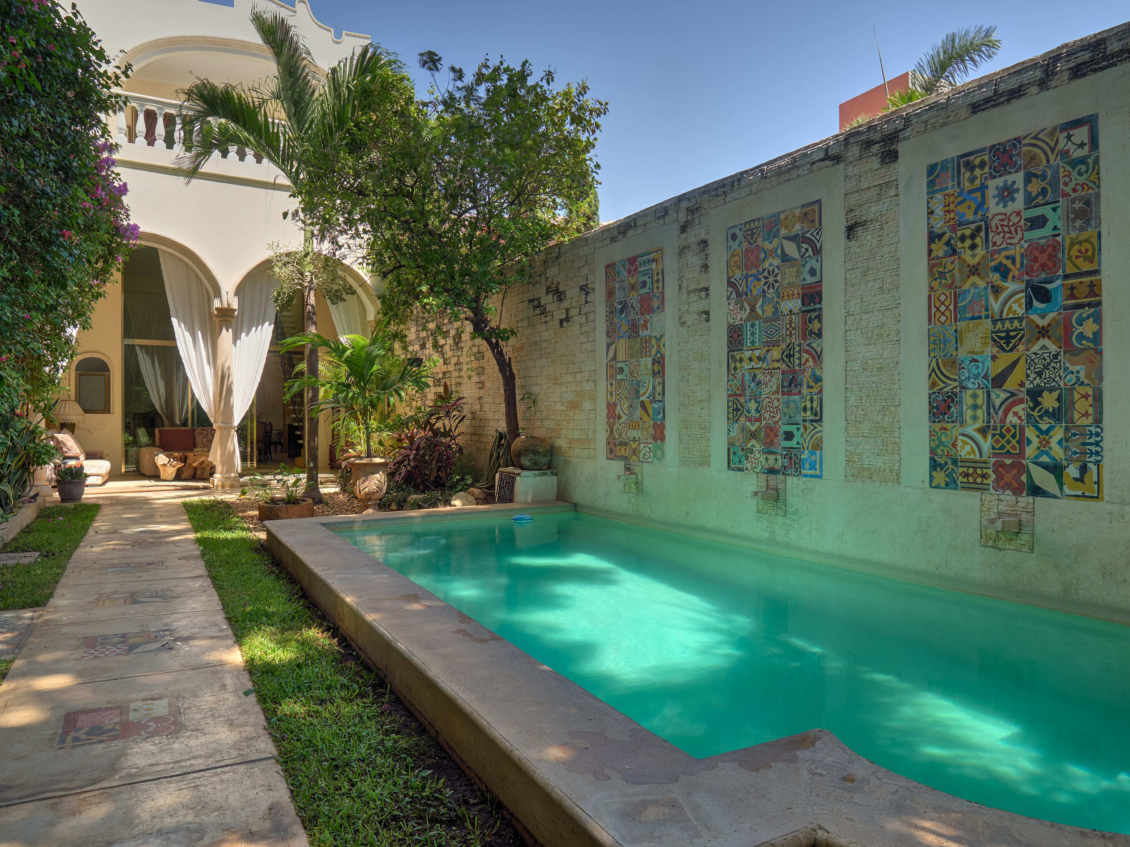 A courtyard with a swimming pool, a covered seating area, and a wall decorated with colorful tiles.