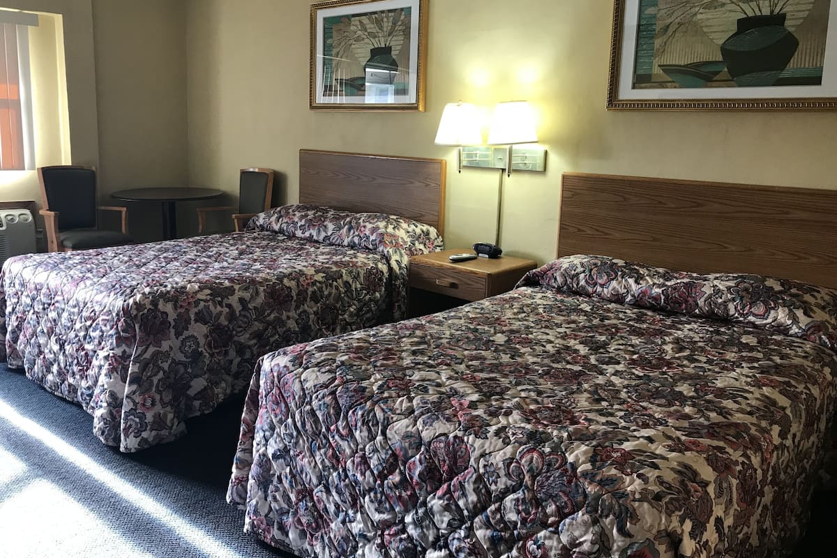Hotellihuone, jossa on kaksi sänkyä, työpöytä, tuoli, lamppu ja kaksi kehystettyä taideteosta seinällä.