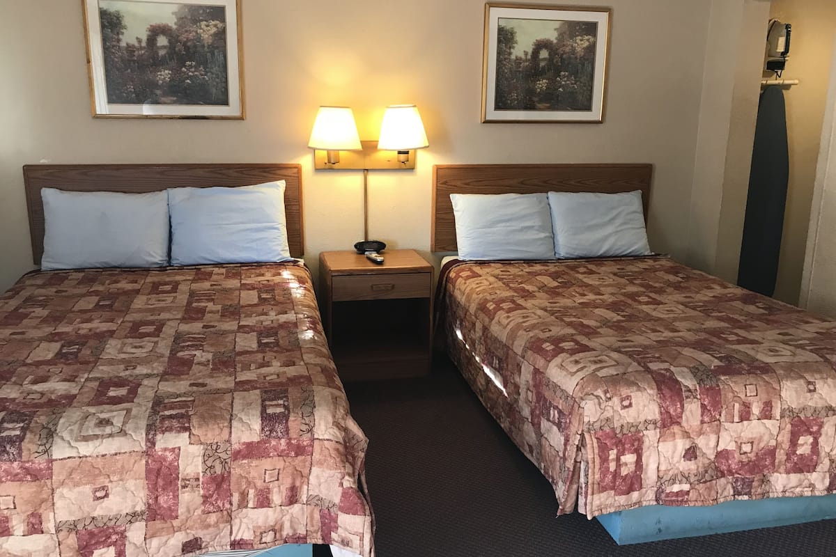 Hotellihuoneessa on kaksi sänkyä, joissa on molemmissa kuviollinen peitto, kaksi seinälle asennettua lamppua ja kaksi kehystettyä kuvaa sänkyjen yläpuolella.
