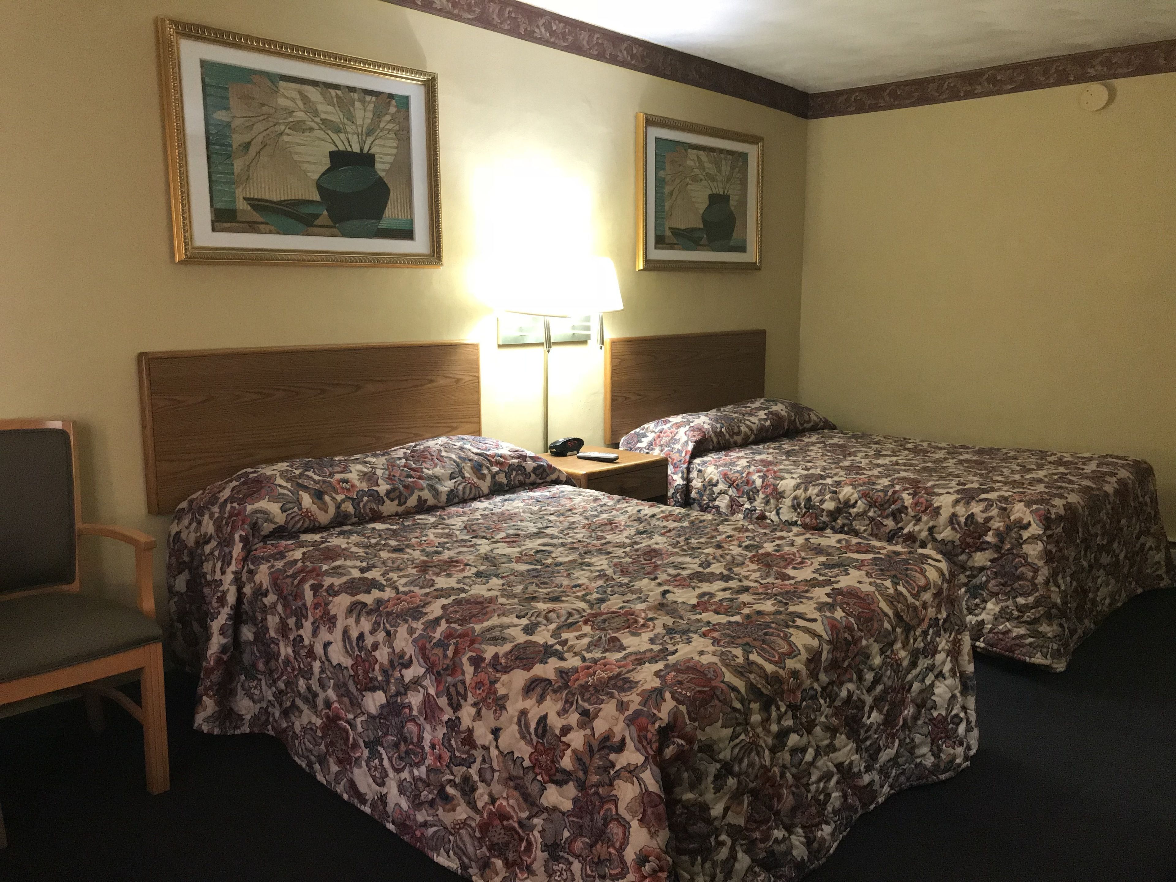 A hotel room with two beds, a nightstand, a lamp, and two framed pictures on the wall.