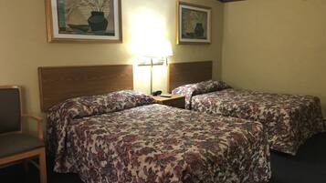 A hotel room with two beds, a nightstand, a lamp, and two framed pictures on the wall.