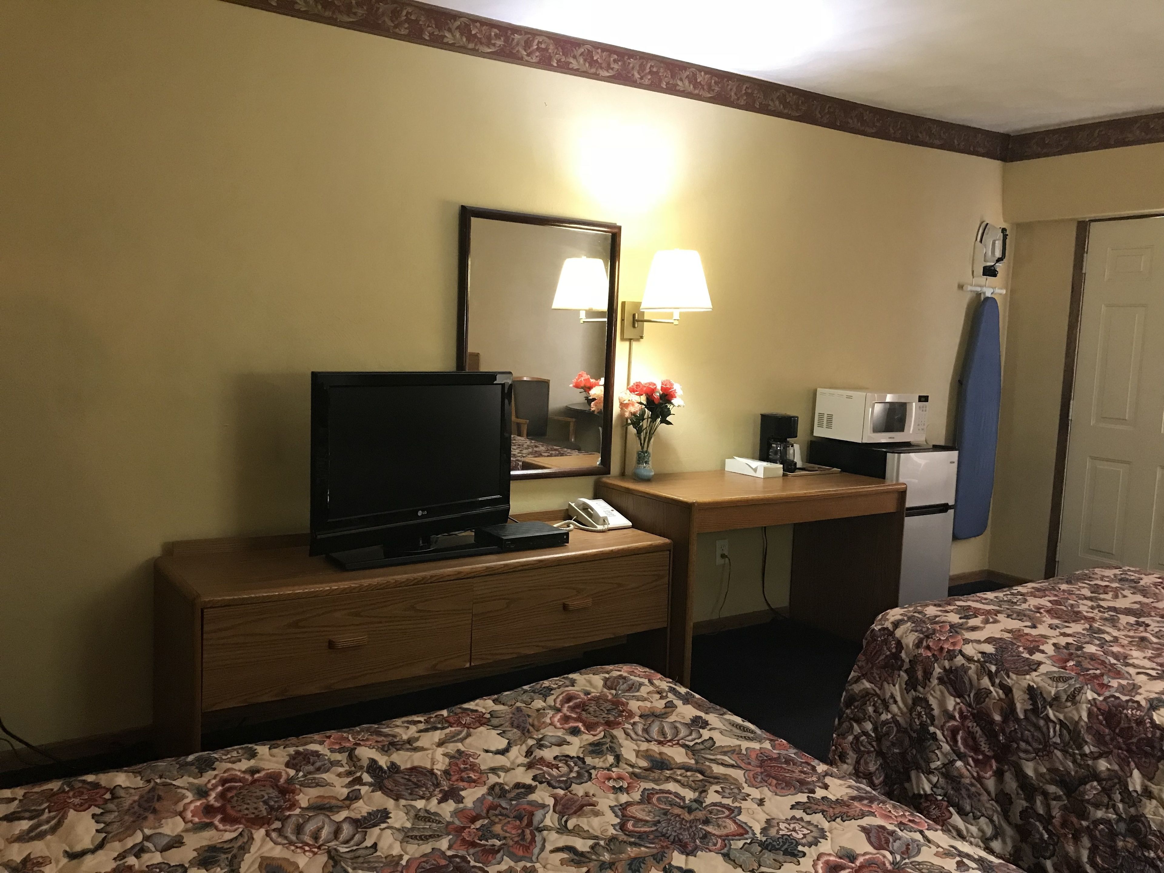 Una habitación de hotel con dos camas, un escritorio, una televisión de pantalla plana, una lámpara, un microondas y un refrigerador pequeño.