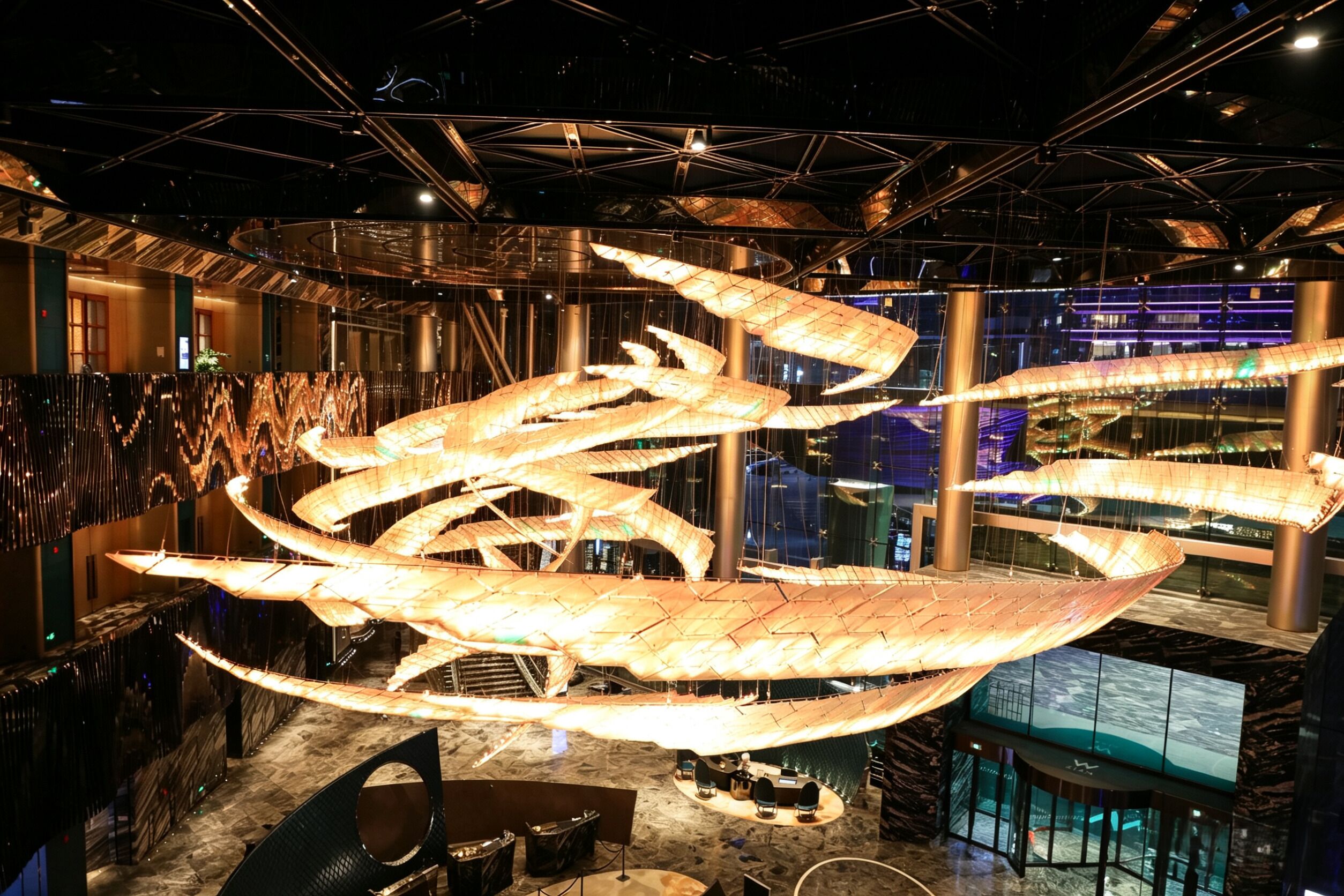 Un interior moderno con una gran escultura iluminada, un techo alto con vigas metálicas y vistas de la ciudad a través de amplias ventanas.