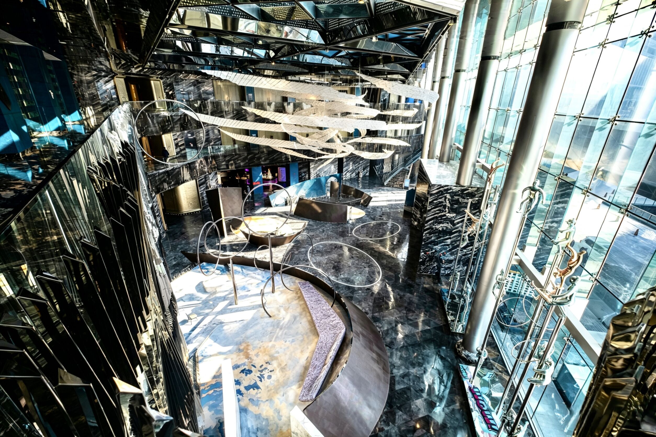 A modern atrium with a curved seating area, reflective surfaces, and a central chandelier.