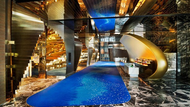A modern interior with a central glass staircase, a reflective floor, and a curved seating area.