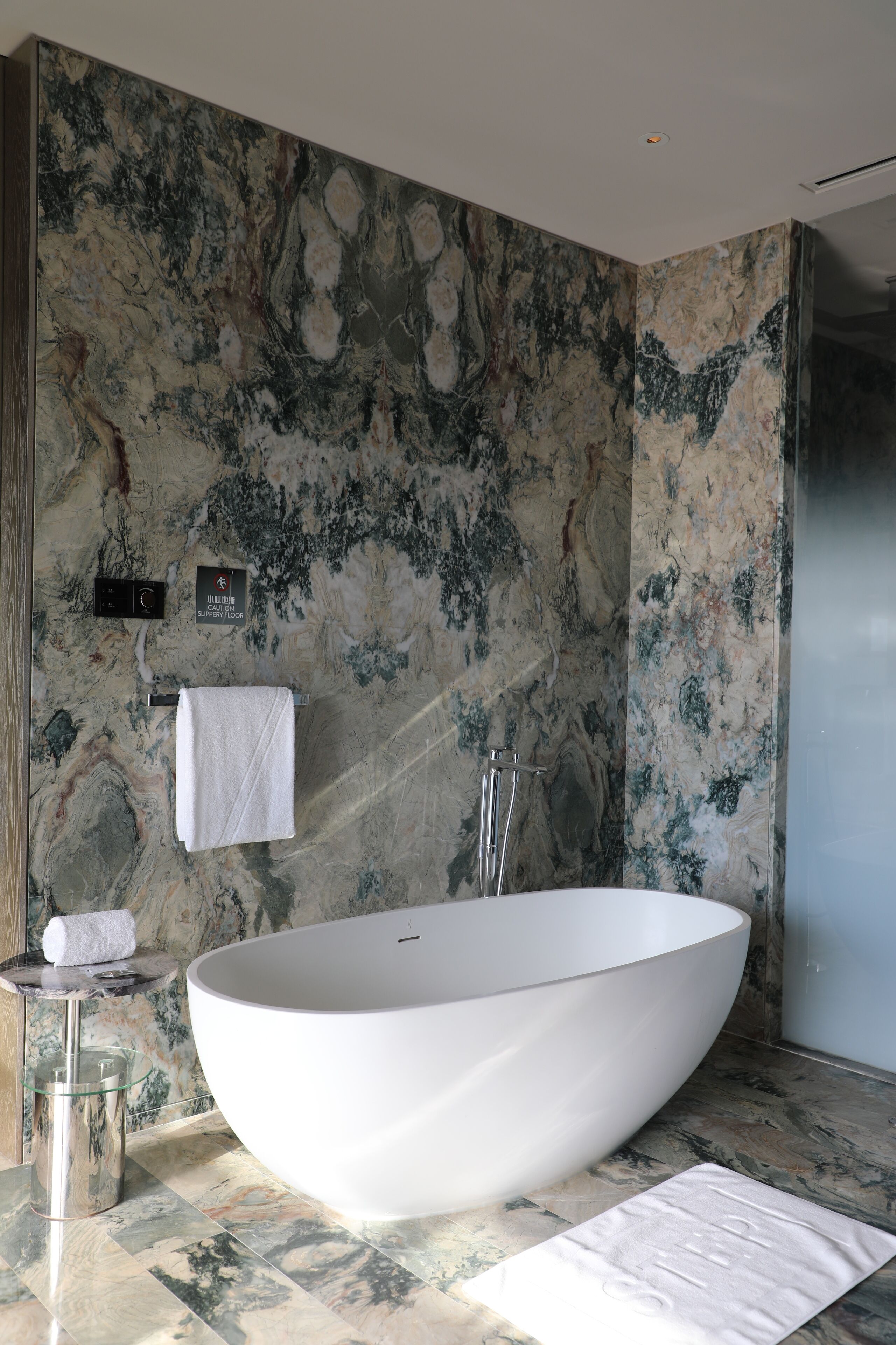 Une salle de bain moderne avec une grande baignoire sur pieds, des murs en marbre, un lavabo en verre et un porte-serviettes.