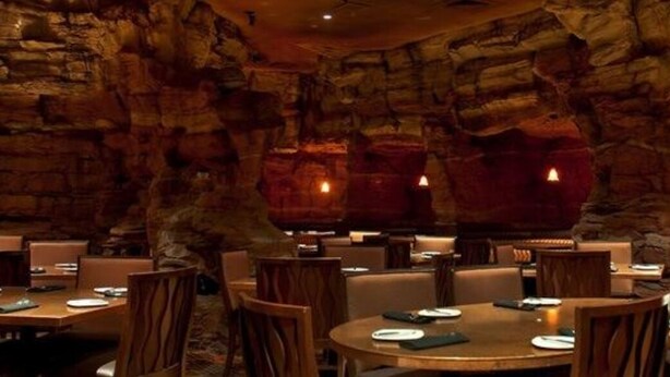 Un restaurant dont les tables et les chaises sont disposées dans un décor évoquant une grotte, avec des formations rocheuses en arrière-plan.