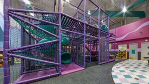 Un espace de jeux intérieur comprenant une structure d’escalade, un toboggan et un sol à carreaux.