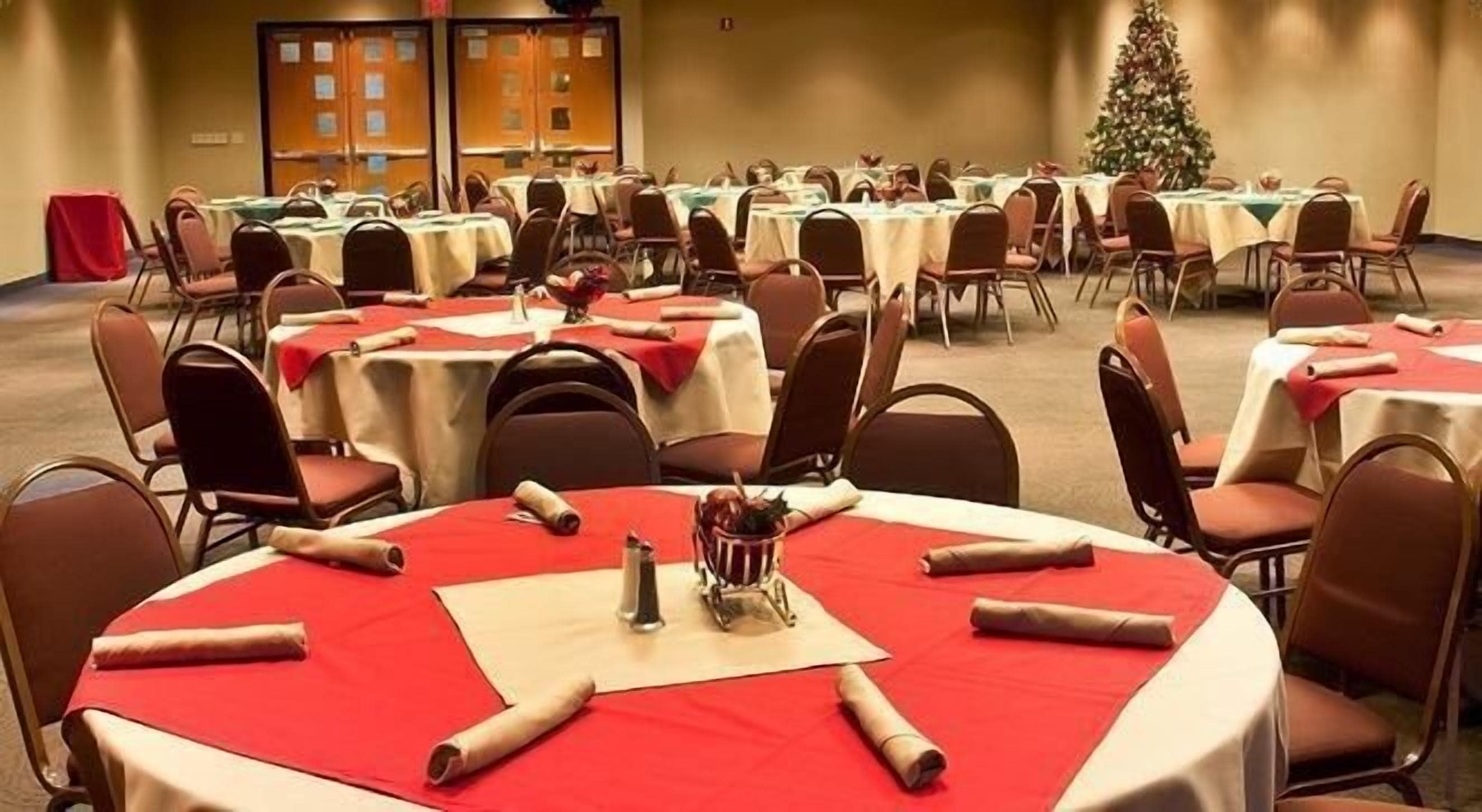A banquet hall with round tables covered in red tablecloths, arranged in rows.