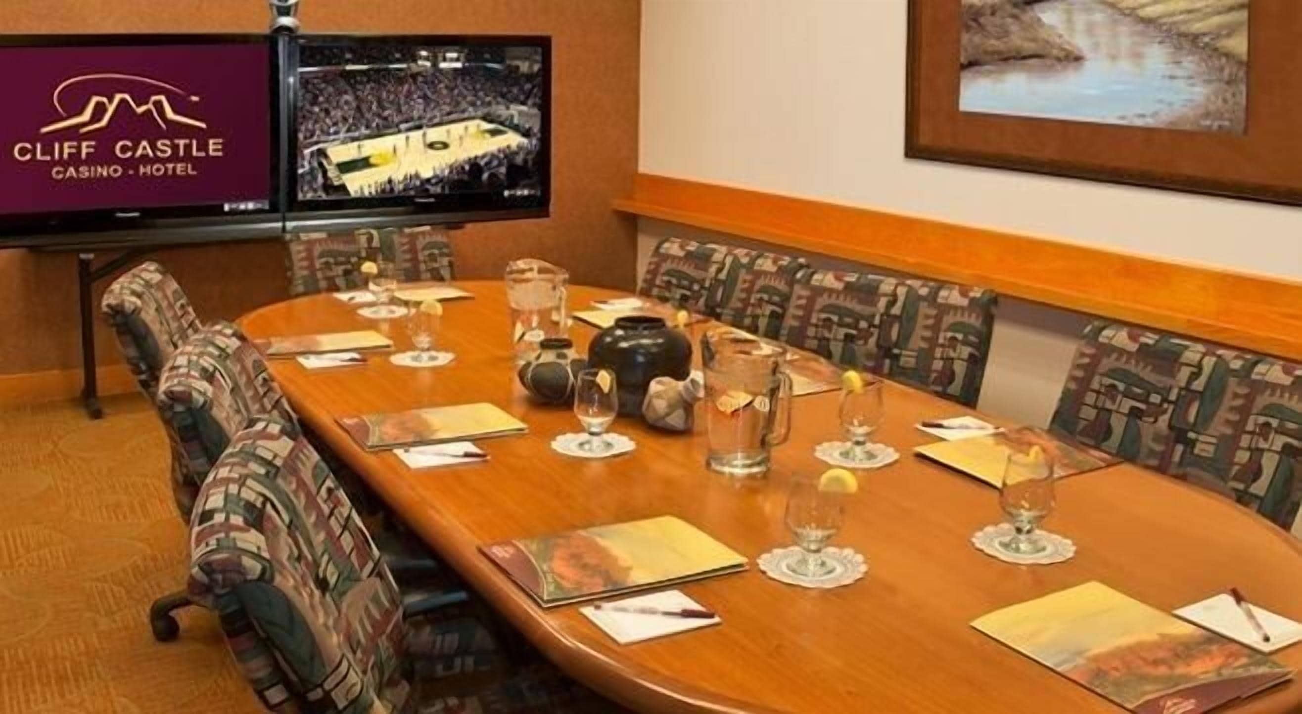 A conference room at Cliff Castle Casino Hotel with a long wooden table, chairs, and a television displaying a sports event.