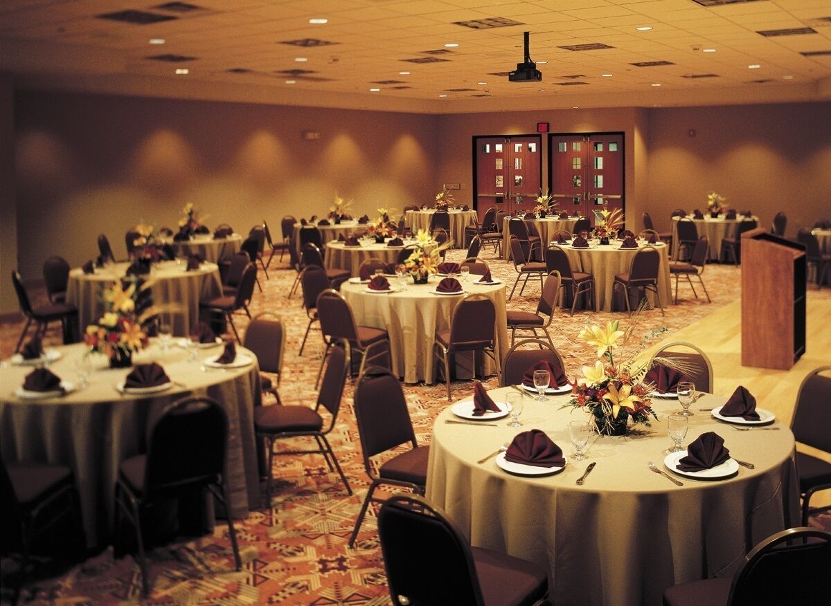 A banquet hall with round tables, chairs, and floral centerpieces.