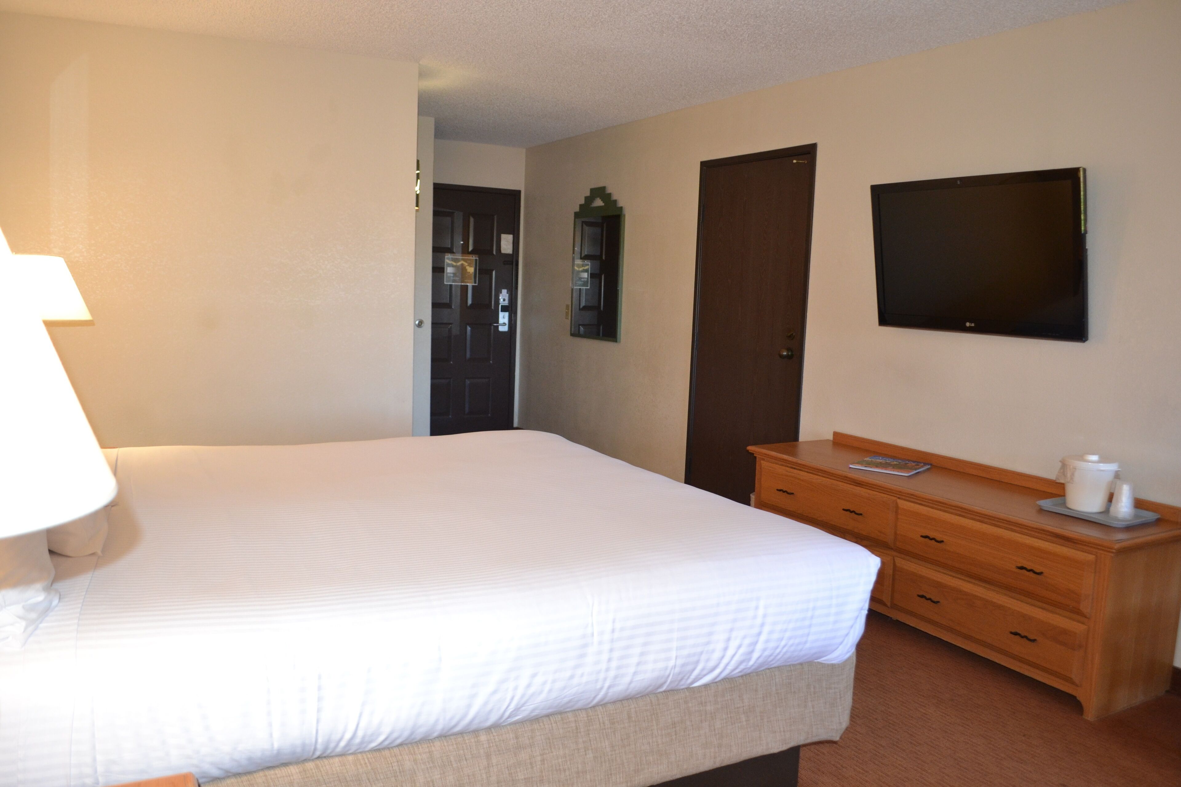 A hotel room with a bed, a wooden dresser, a television, and a door.