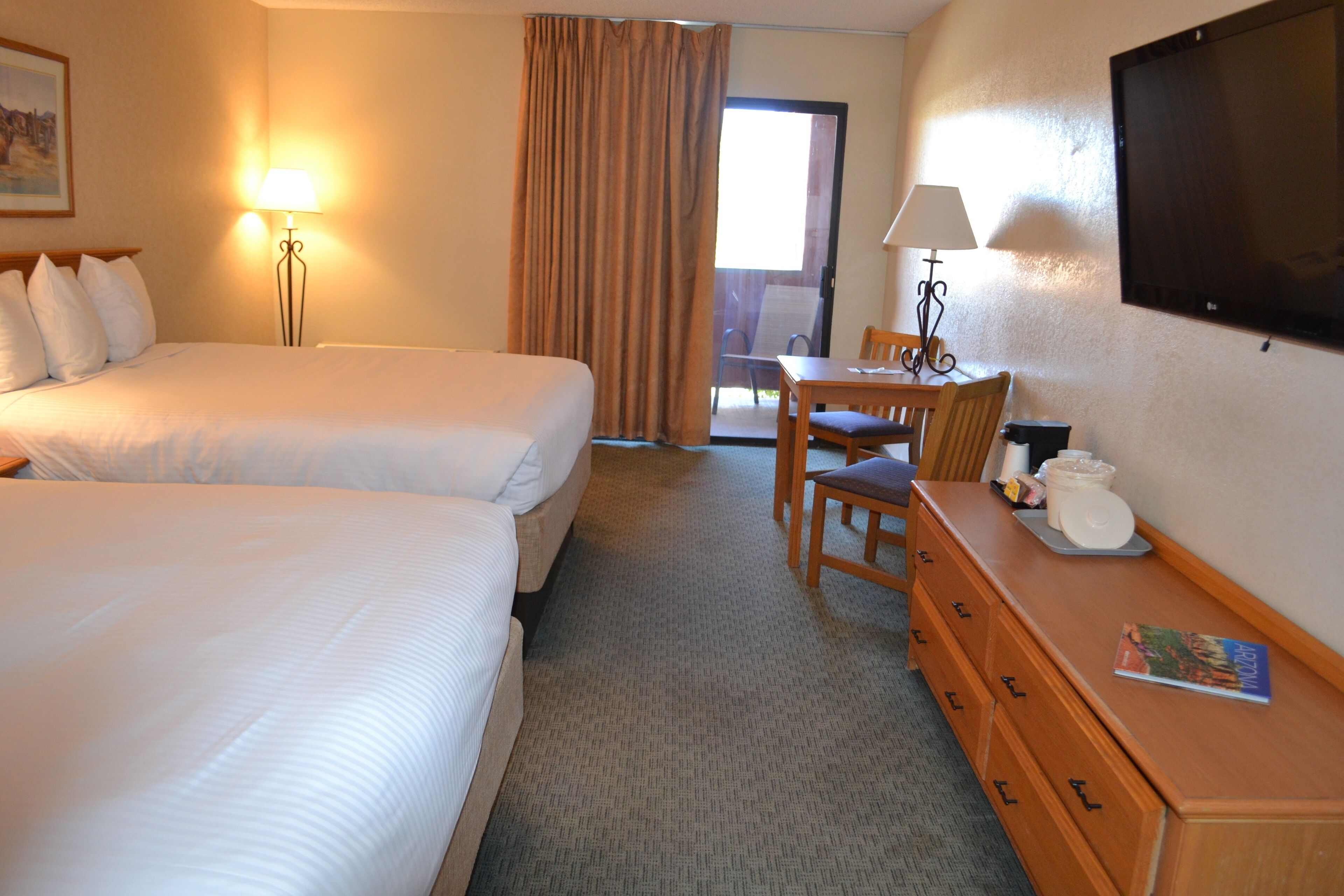 A hotel room with two beds, a desk, a chair, a dresser, and a TV.