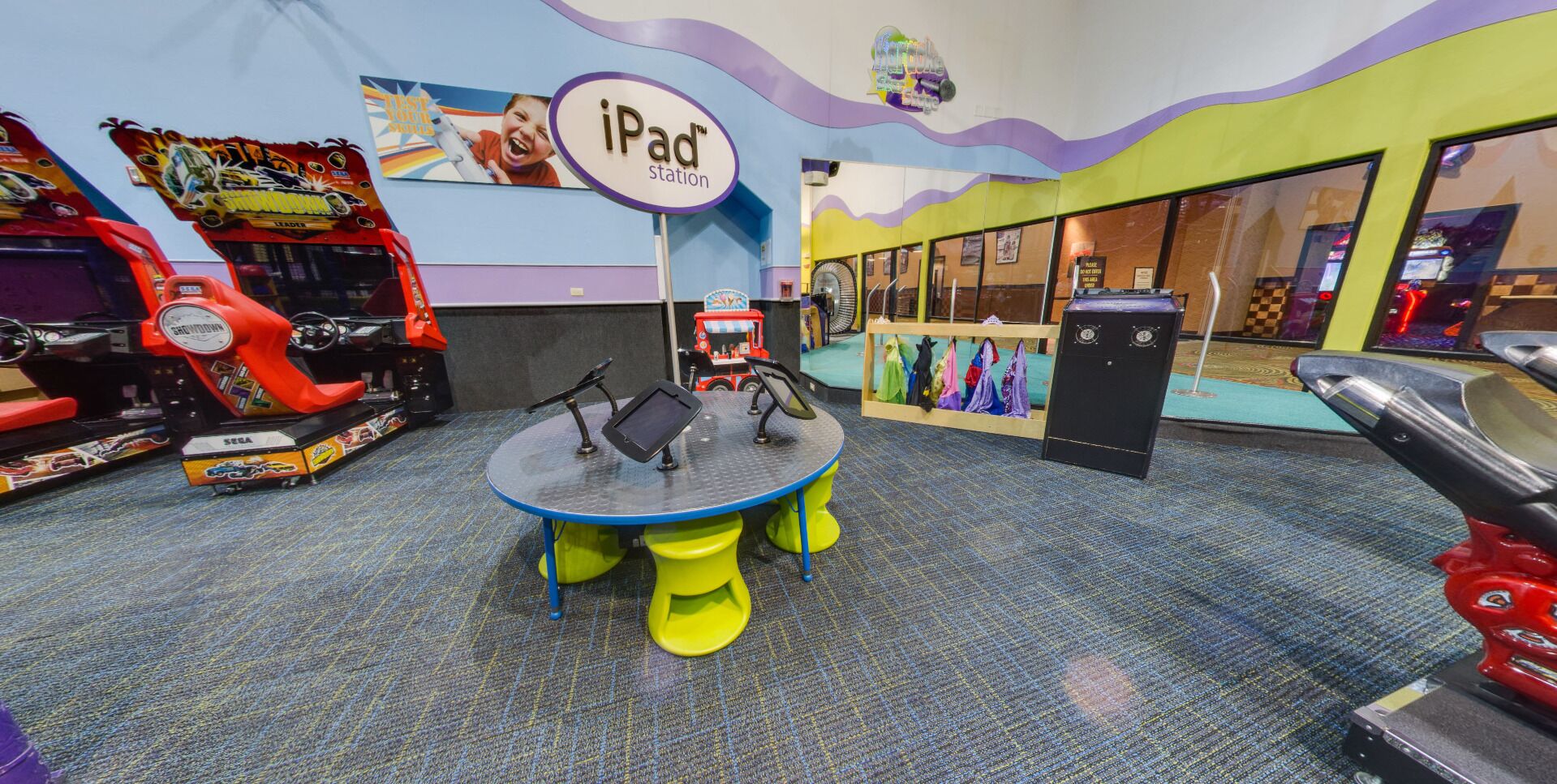 An indoor play area with a table for iPad use, arcade games, and a toy food truck.