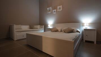 Un dormitorio con una cama grande, un sofá cama más pequeño, dos mesitas de noche con lámparas y tres cuadros en la pared.