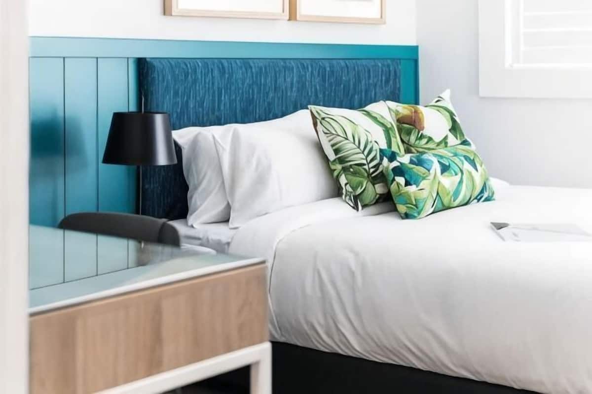 A hotel room with a bed, a desk, a lamp, and a window.