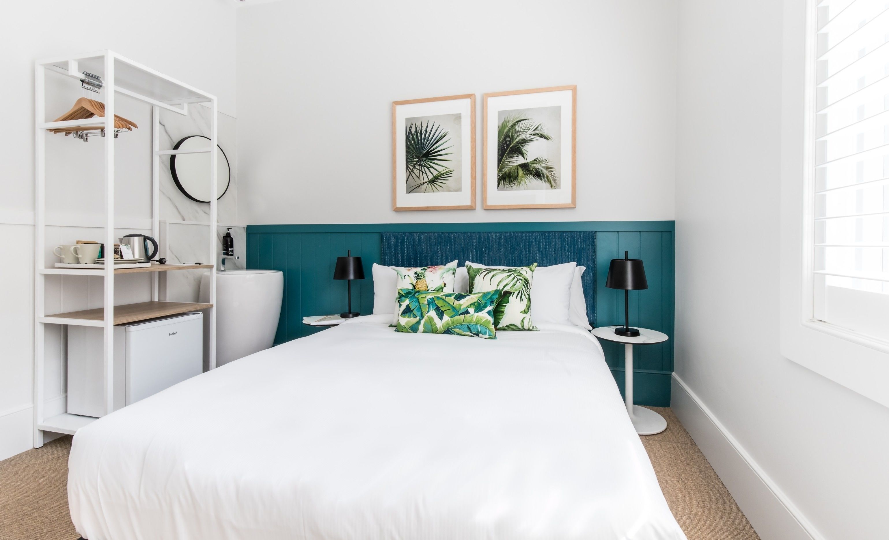 A neatly arranged bedroom with a bed, bedside tables, a wardrobe, and two framed tropical plant pictures on the wall.