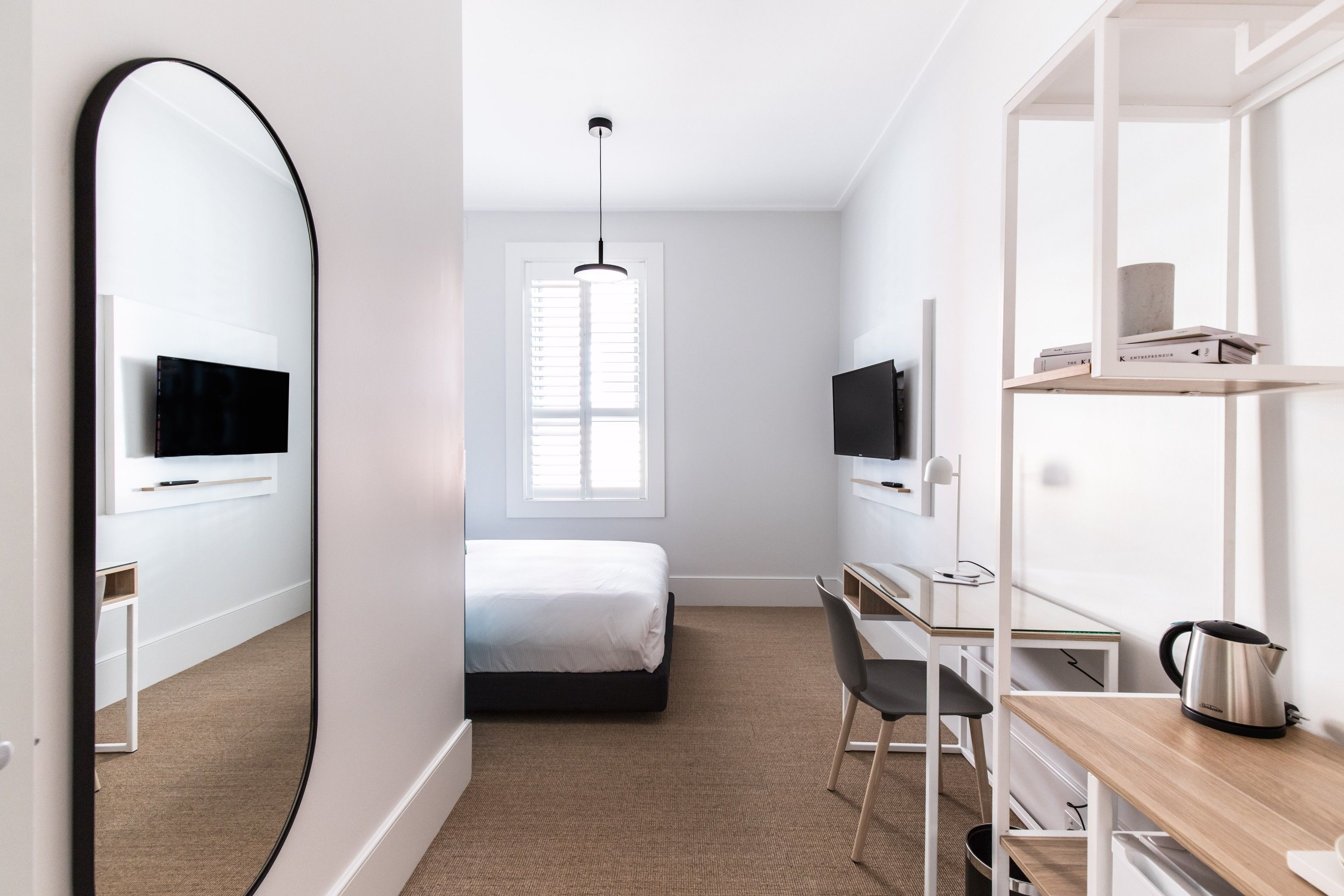 A modern bedroom with a bed, a desk, a chair, a TV, and a large mirror.