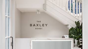 Een receptiegedeelte met een trap, een bordje aan de muur met de tekst 'THE BAXLEY BONDI' en een potplant.