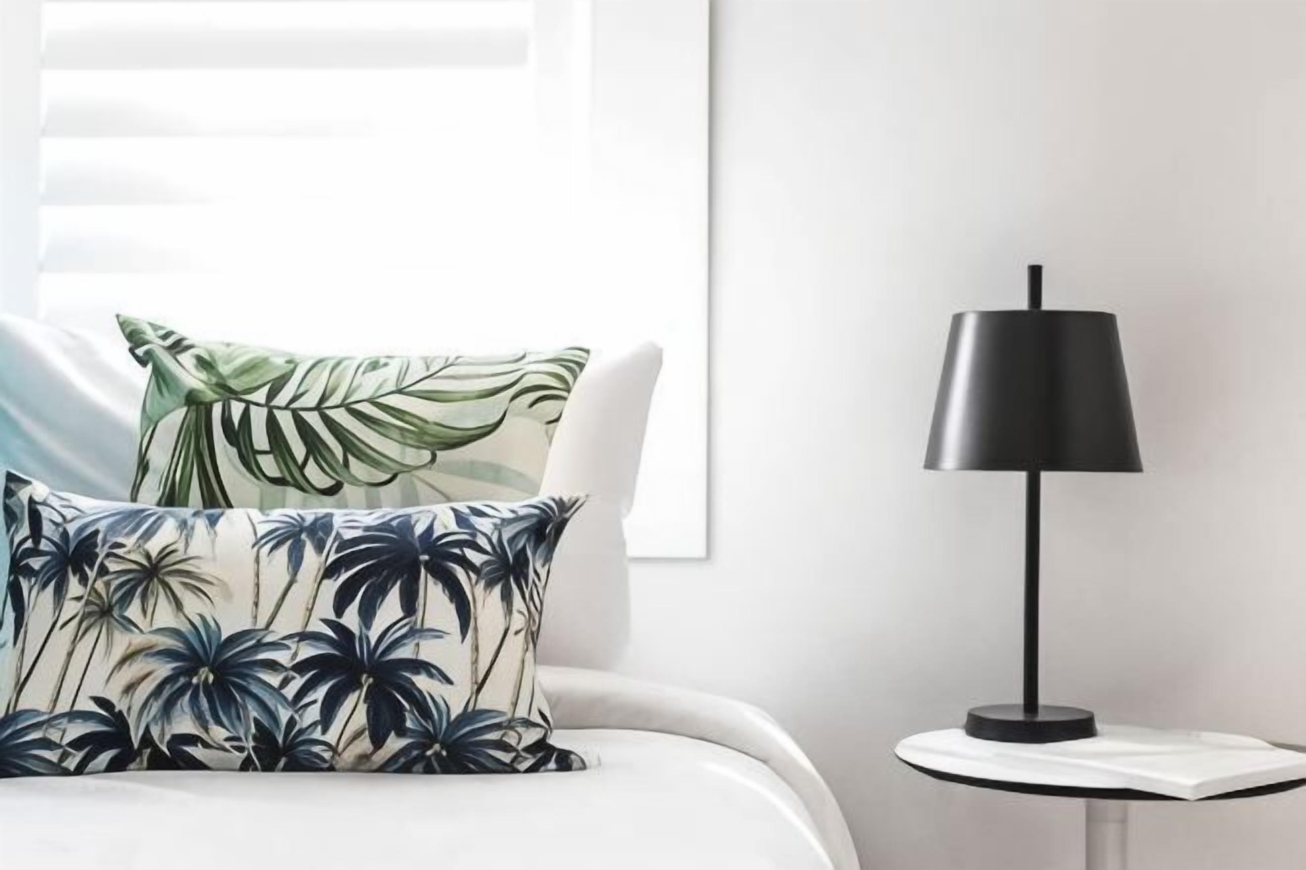 Un lit avec un oreiller, une table de chevet avec une lampe et une fenêtre avec des stores.