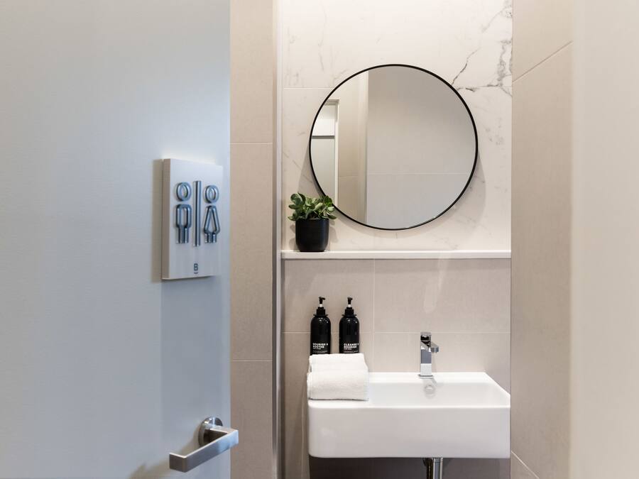 A modern bathroom with a white sink, a round mirror, and two bottles of shampoo.