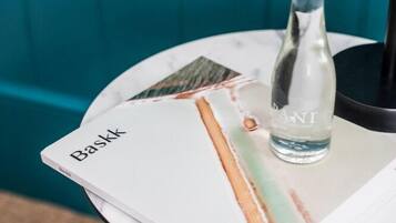 A bottle of water on a table with a book titled 'Baskk' and a black object in the background.