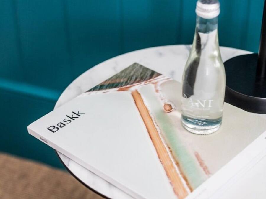 A bottle of water on a table with a book titled 'Baskk' and a black object in the background.
