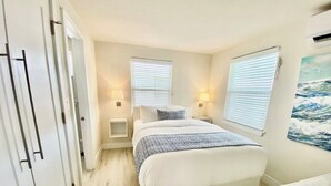 A bedroom with a bed, bedside tables, a wardrobe, and a painting on the wall. - Amazing NEW 1BR APT just Steps to the Beach! Unit 312 (Cocoa Beach)