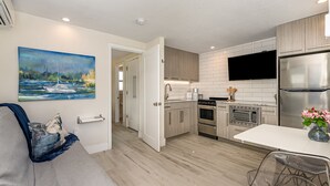 A modern kitchen with white cabinets, stainless steel appliances, and a flat-screen TV. - Amazing NEW 1BR APT just Steps to the Beach! Unit 312 (Cocoa Beach)