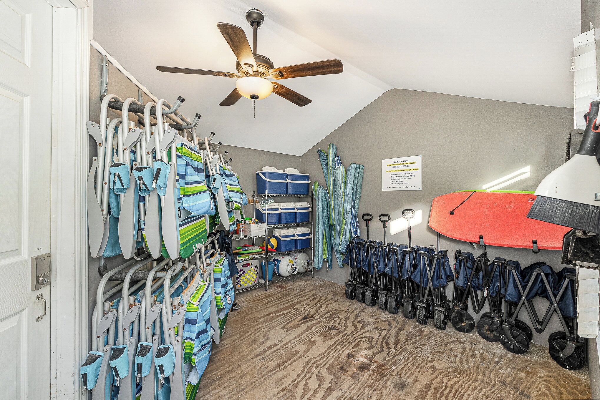 A room with a ceiling fan, storage shelves with luggage, and a surfboard.