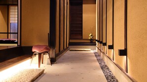 A hallway with a wooden bench, a small table with a vase, and a staircase leading to a room. - Houka (Kyoto)