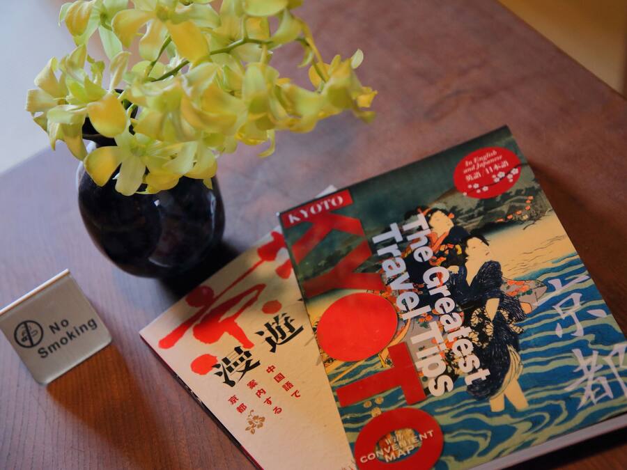 Een tafel met een vaas gele bloemen, een ‘Niet Roken’ bord en een boek getiteld 'The Greatest Travel Times'.