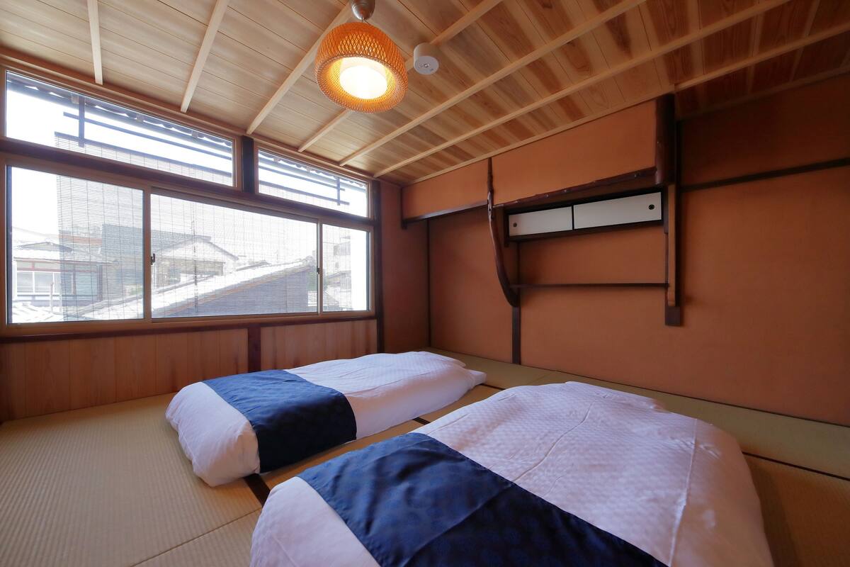 Una habitación con dos camas, techo de madera, un ventanal grande y una lámpara colgante.