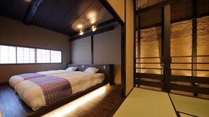 A traditional Japanese-style room with tatami flooring, a low bed with a wooden headboard, and a sliding door with a textured wall. - Houka (Kyoto)