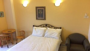 Une chambre bien rangée, avec un lit, deux lampes fixées au mur, un tableau encadré, une petite table ronde et deux chaises.