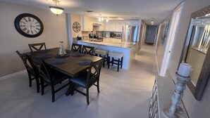 A modern kitchen with a central island, a dining area with a wooden table and chairs, and a clock on the wall. - Direct Gulf Front Las Brisas 105, Very Nicely Updated 3 Bedroom/2 Bath (Madeira Beach)