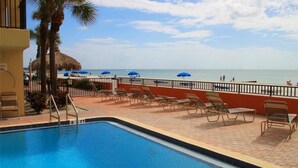 A pool area with lounge chairs and umbrellas, a palm tree, and a view of the beach. - Direct Gulf Front Las Brisas 105, Very Nicely Updated 3 Bedroom/2 Bath (Madeira Beach)