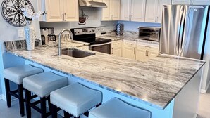 A modern kitchen with a marble countertop, stainless steel appliances, and a bar area with stools. - Direct Gulf Front Las Brisas 105, Very Nicely Updated 3 Bedroom/2 Bath (Madeira Beach)