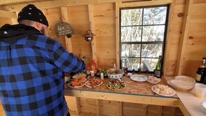 A wooden cabin interior with a dining table set for a meal, a window with a view of trees, and a sign on the wall. - Peaceful lakeside private waterfront campsite; 45 min drive to Acadia! BYOTent (Eastbrook)