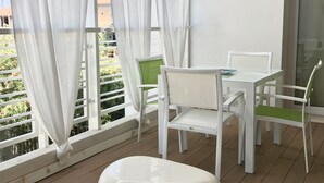 Un balcó amb taula i cadires blanques, una otomana blanca i cortines blanques.