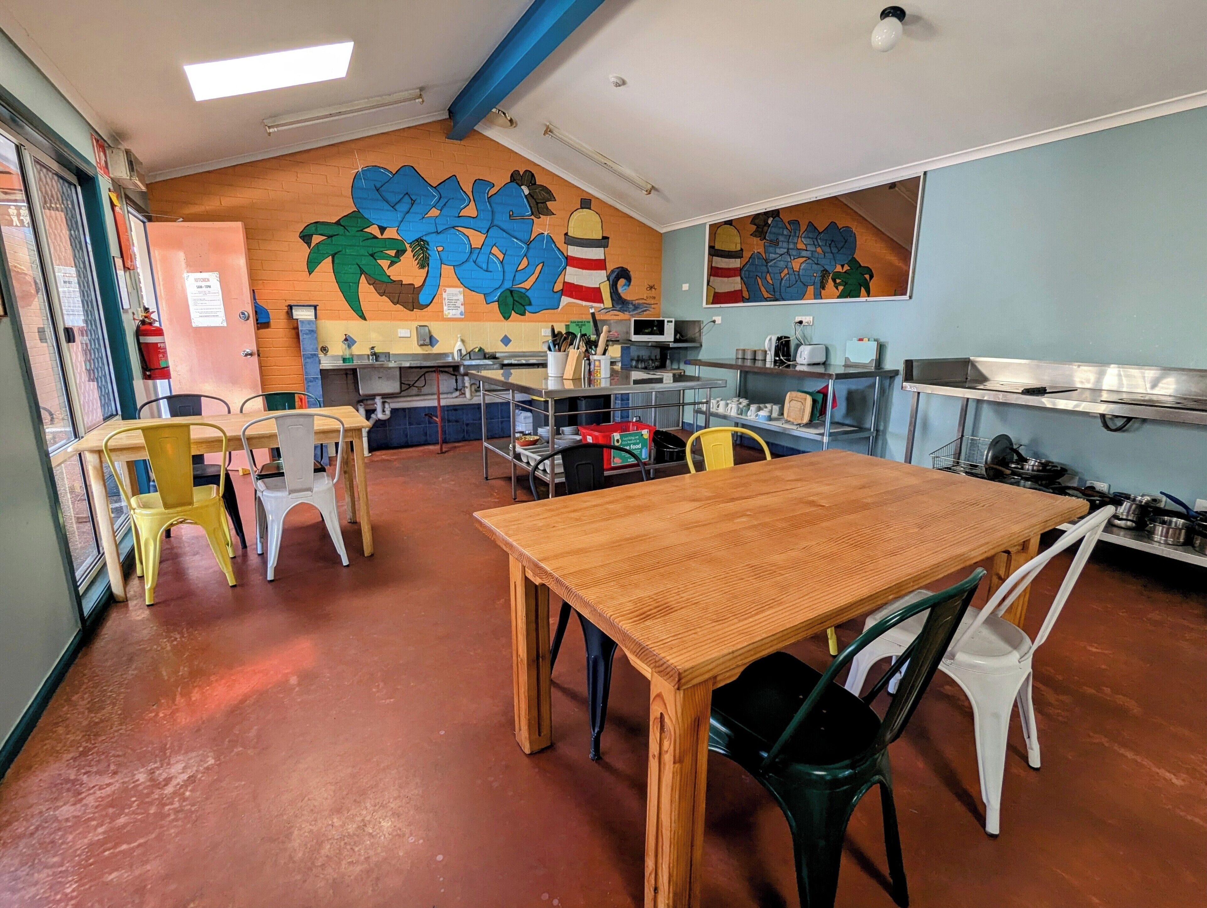 A restaurant with a wooden table and chairs, a kitchen area, and a colorful mural on the wall.