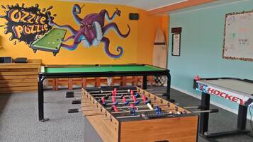 Una habitación con mesa de futbolín, mesa de billar y un mural en la pared.